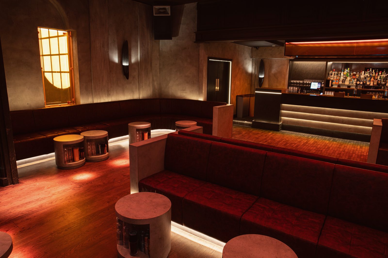 The Club Room towards the arched amber window and the bar, red banquettes and drum tables in front