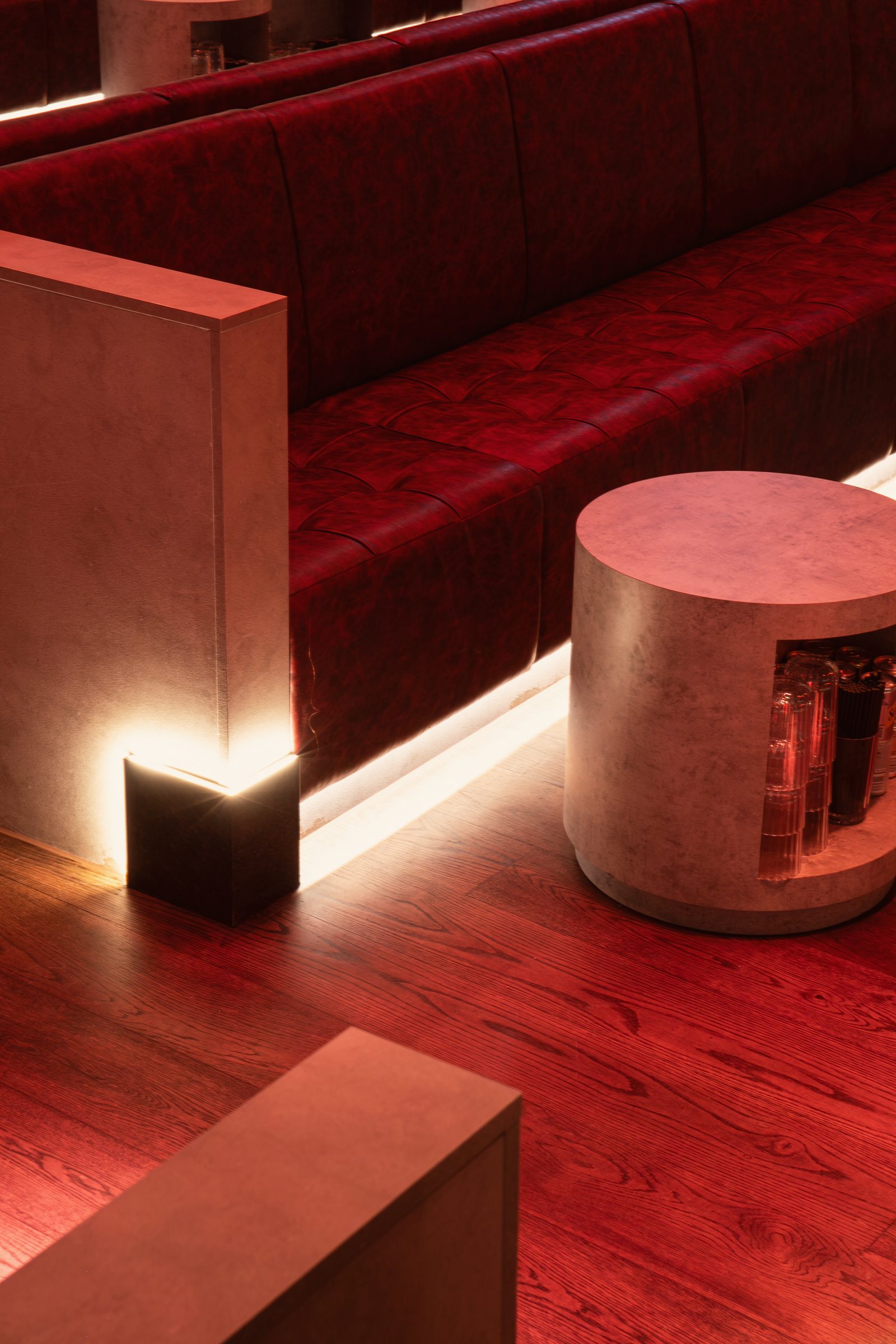 Tufted red leather banquettes and a concrete drum table in the Club Room, lit from below