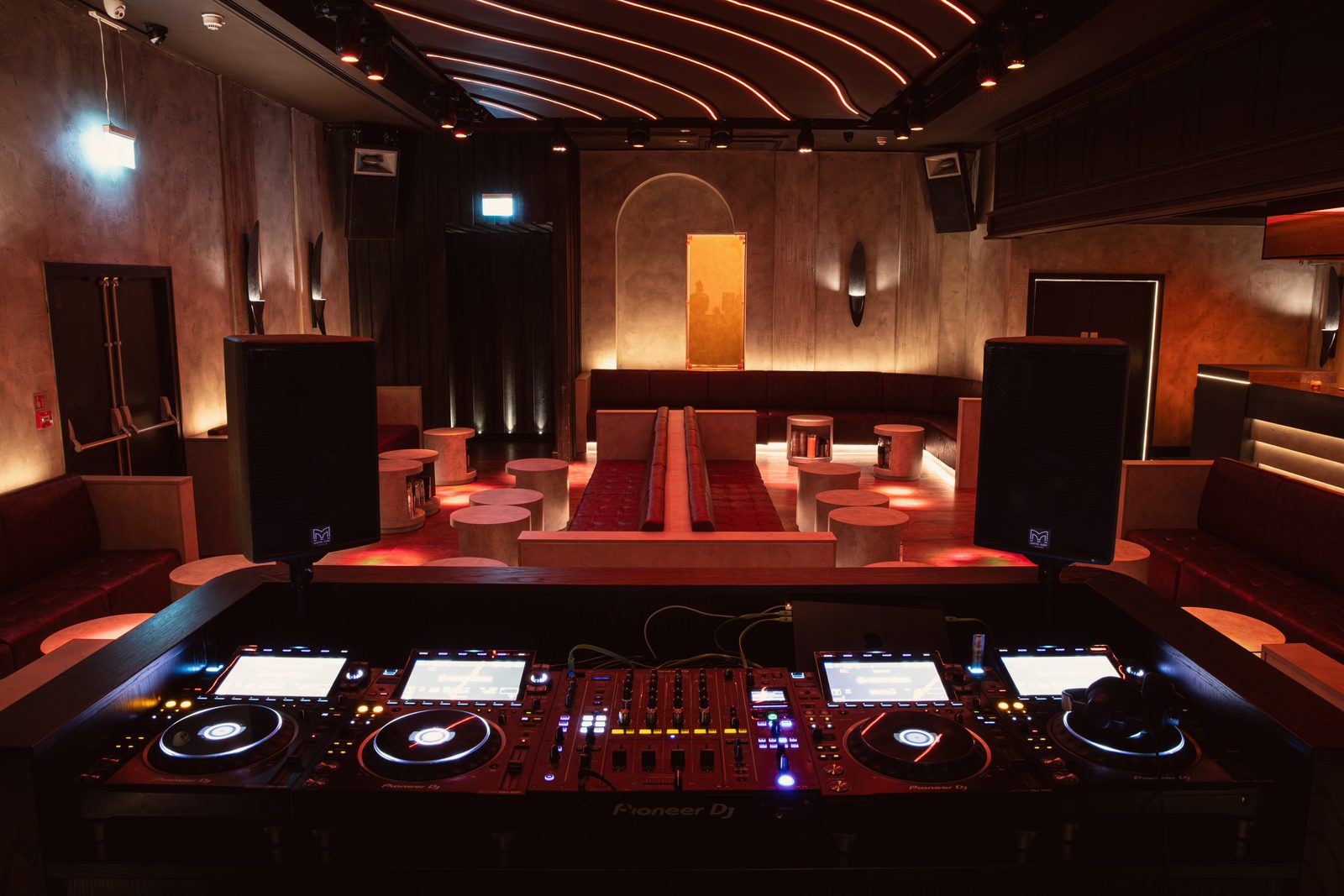 The Club Room from behind the decks, looking over the banquettes and drum tables to an amber panel glowing in an arched niche