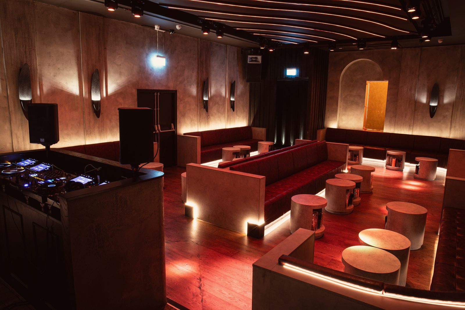 The Club Room, lit and empty: red leather banquettes and concrete drum tables running to an amber panel in an arched niche