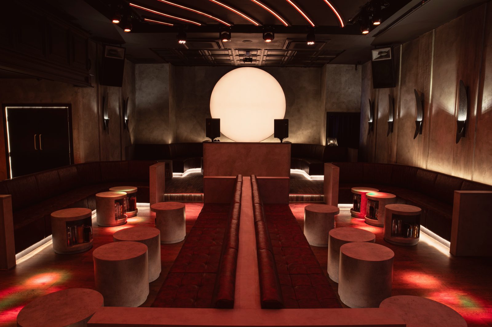 The Club Room at NinetyNine: the sun glowing behind the DJ booth, red leather banquettes and concrete drum tables either side