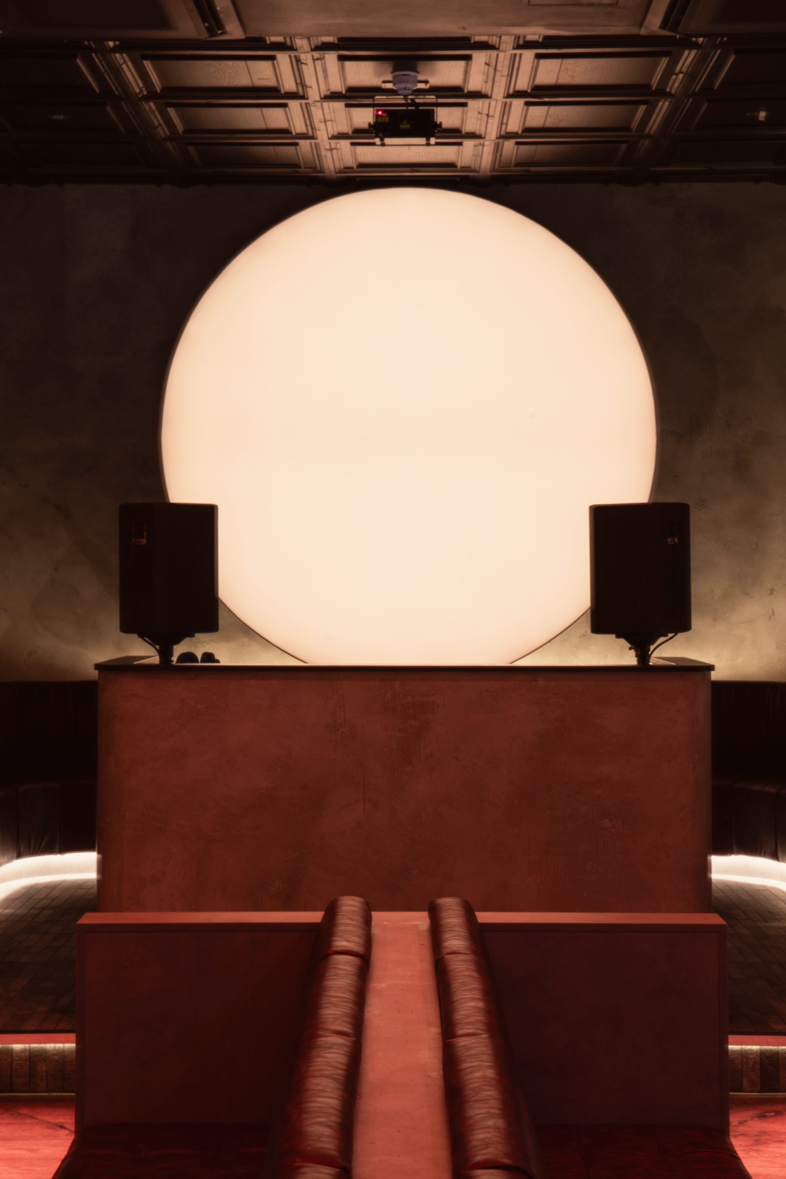 The sun behind the DJ booth, two speakers either side and the leather banquettes leading to it