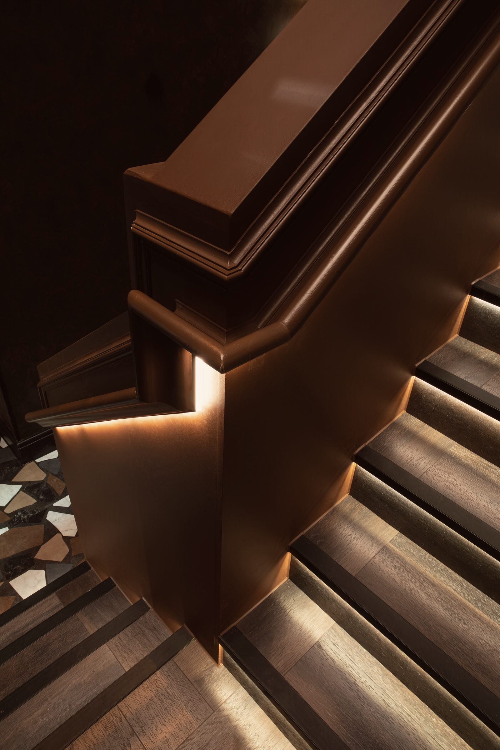 The bronze handrail turning at the foot of the stairs, above a terrazzo floor