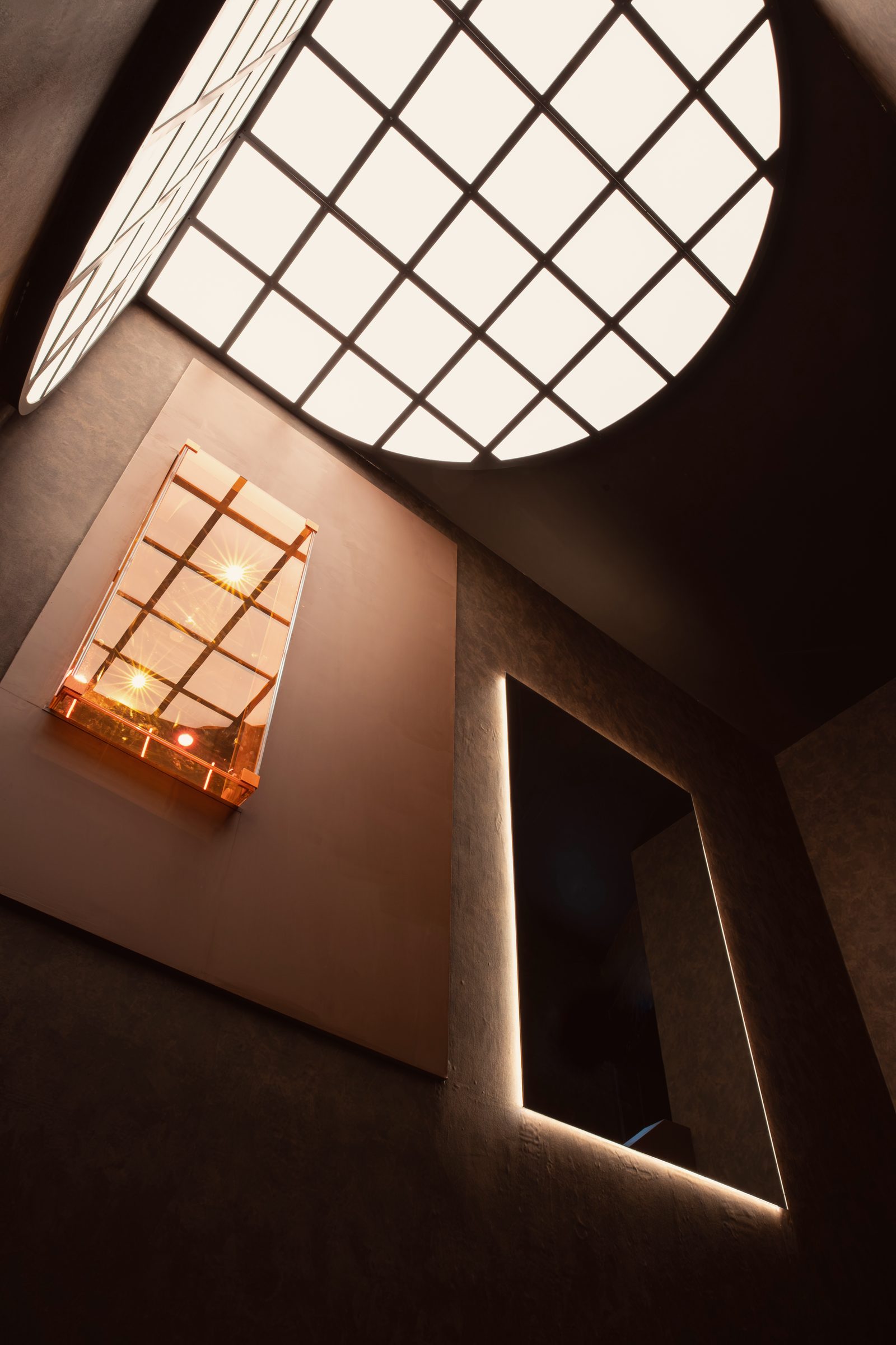 Looking up the stairwell to a round gridded skylight and an amber light box