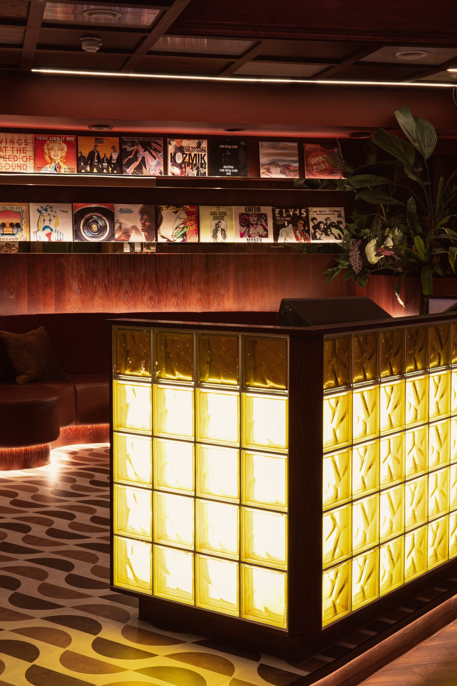 The Vinyl Room: the glass-block DJ booth glowing amber beneath a wall of record sleeves